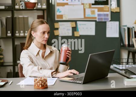 Femme adulte travaillant sur ordinateur portable tout en buvant du café dans le bureau Banque D'Images