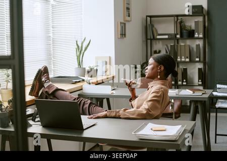 Femme adulte noire se relaxant tout en enregistrant un message vocal au bureau Banque D'Images