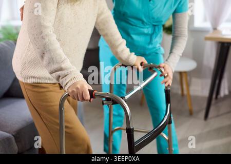Femme âgée utilisant un déambulateur avec soutien infirmier à domicile pour les soins de rééducation à mobilité réduite Banque D'Images