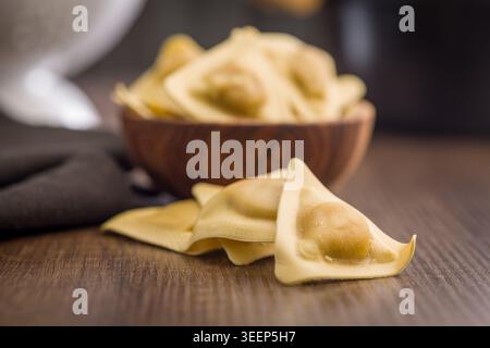 Pâtes de raviolis fraîches non cuites disposées sur une table en bois avec un bol rustique au focus doux, évoquant la cuisine italienne maison, la préparation artisanale des aliments Banque D'Images