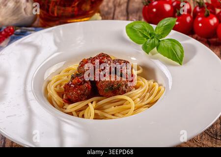 Boulettes de viande italiennes classiques à spaghetti servies dans une assiette blanche. Sauce rouge riche, feuille de basilic vert vif, tomates cerises fraîches, piment, complème à l'ail Banque D'Images