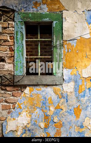 Gros plan d'un cadre de fenêtre rustique en bois vert altéré installé dans un mur texturé coloré et pelable, Ipoh, Perak, Malaisie Banque D'Images