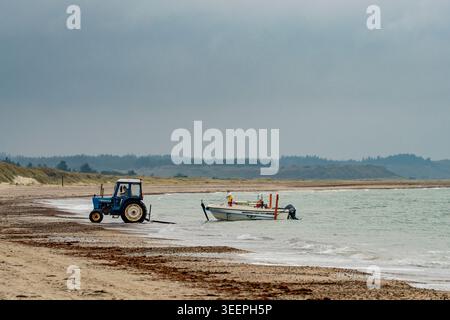 Par un jour nuageux gris couvert, un pêcheur professionnel solitaire ramène son petit bateau dans la mer du Nord à Thorup Strand à Demark Banque D'Images