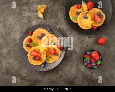 Composition aérienne de crêpes avec des fraises, des baies et des agrumes sur fond sombre texturé Banque D'Images