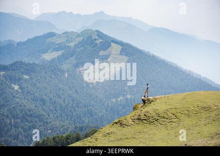 Un randonneur solitaire se tient sur une crête de montagne herbeuse surplombant une vaste vallée, Raghupur Fort, Sojha, Manali, Himachal Pradesh, Inde. Banque D'Images