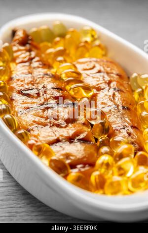 Filets de maquereau fumé avec capsules d'huile de foie de morue dans un plat blanc. Concept sain de régime Oméga 3 Banque D'Images