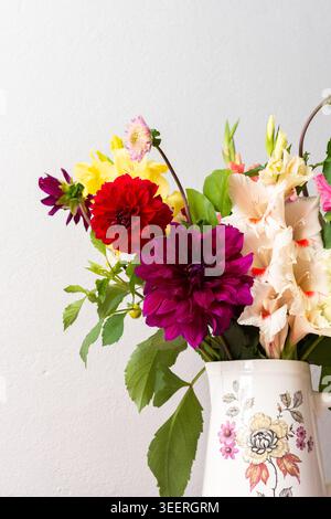 Un vase contient une variété de fleurs fraîches avec différentes couleurs. Les fleurs sont placées sur une table rose. Derrière le vase se trouve un mur Uni dans un roo lumineux Banque D'Images