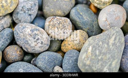 Gros plan sur un tas de roches marines lisses assorties. Textures variées et couleurs subtiles bleues, grises et bronzées sous un éclairage doux. Bon pour les arrière-plans ou natu Banque D'Images