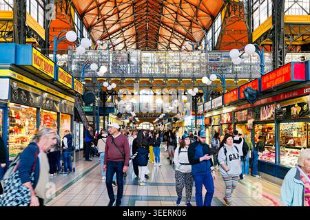 Les gens marchent à travers Central Market Hall à Budapest. Les stands présentent divers aliments et marchandises. Le marché est animé par les acheteurs et les visiteurs. Banque D'Images