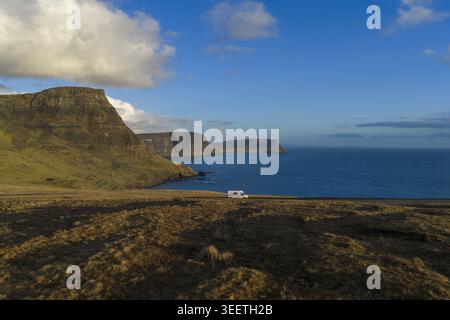 Vue aérienne d'un camping-car garé sur une route côtière surplombant les falaises spectaculaires et l'océan bleu sous un ciel lumineux à l'île de Skye. Banque D'Images