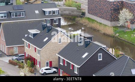 Vue aérienne de maisons résidentielles modernes avec des toits de tuiles sombres et un petit canal à Almere, Flevoland, pays-Bas. Banque D'Images