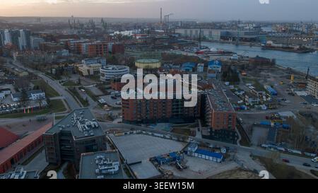 Vue aérienne au crépuscule du front de mer industriel de Gdansk avec bâtiments résidentiels rouges, grues maritimes et infrastructures maritimes Banque D'Images