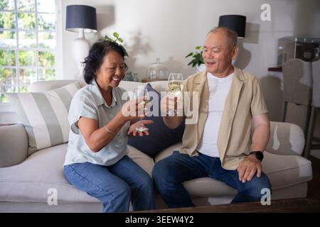 Femme chinoise senior et homme chinois adulte mature serrant des verres à vin tout en étant assis sur un canapé léger Banque D'Images