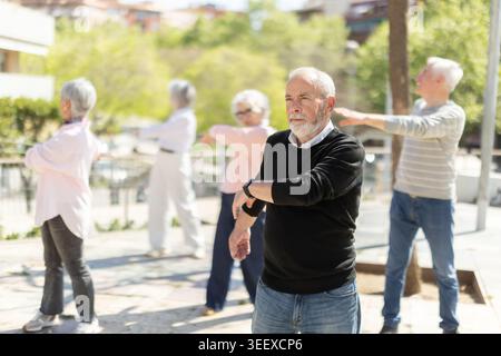 Groupe de personnes âgées pratiquant des exercices de balancement des bras dans la cour Banque D'Images