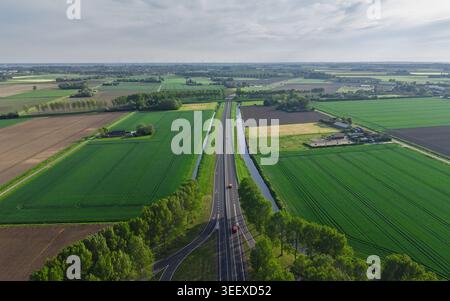 Vue aérienne d'une autoroute droite avec des voitures traversant des champs agricoles verdoyants et des prairies. Banque D'Images