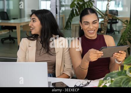 Deux femmes en affaires portent réagissant au message drôle de tablette tout en riant au bureau Banque D'Images