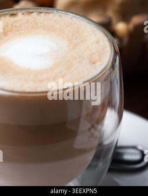Le verre contient un latte crémeux avec un dessus en mousse lisse. Les tons chauds suggèrent le confort et la détente calme. Le café se trouve à côté des biscuits flous, évoquant une friandise sucrée Banque D'Images