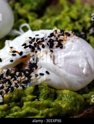 Des restes crémeux d'oeufs pochés sur la purée d'avocat. Les graines de sésame noir et blanc ajoutent texture et contraste. Riche et verte, la pâte à tartiner invite à un petit déjeuner sain. S Banque D'Images