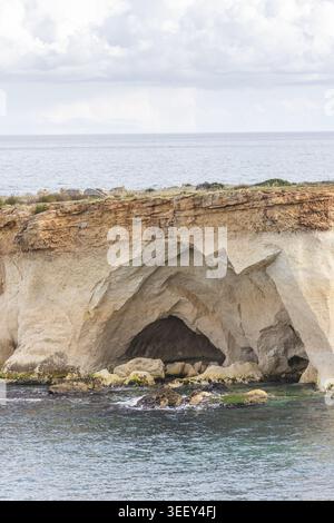 Vue d'une grande grotte marine creusée dans une falaise de calcaire accidentée le long de la côte méditerranéenne sous un ciel nuageux Syracuse, Sicile, Italie. Banque D'Images