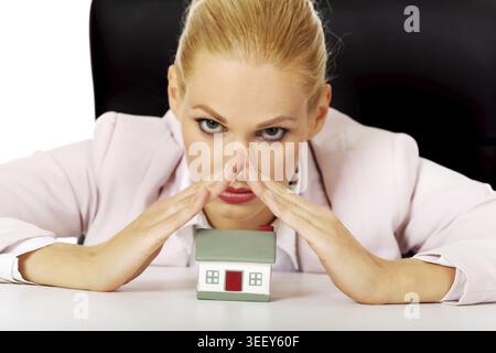 Femme d'affaires assise derrière le bureau avec modèle de maison Banque D'Images