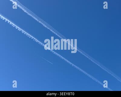 Des traînées d'avion à haute altitude créant des lignes diagonales dynamiques à travers un ciel bleu clair. Expérience minimale de l'aviation avec voyage, transport, cli Banque D'Images
