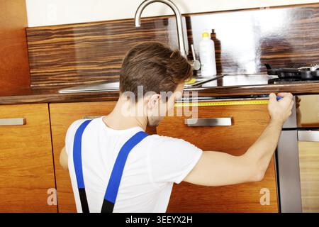 Jeune réparateur mesurant l'armoire de cuisine Banque D'Images