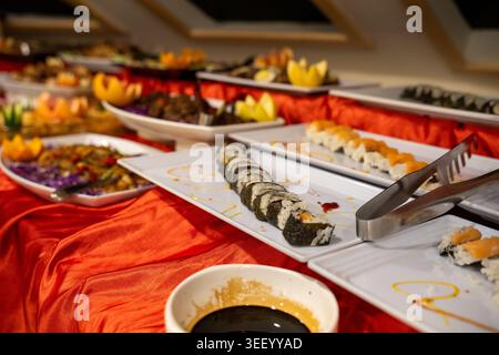 Assortiment de sushis et divers plats asiatiques disposés sur une ligne de buffet avec une nappe rouge Banque D'Images