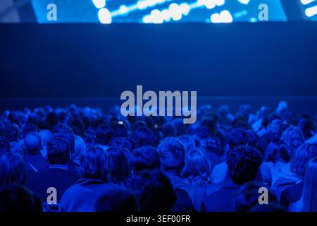 Grand public regardant la présentation dans la salle de conférence bleu foncé, atmosphère d'événement d'entreprise, attention et anticipation concentrées. Banque D'Images