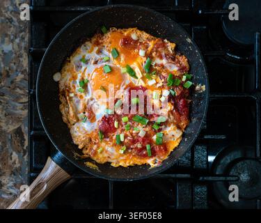 Une poêle vibrante de shakshuka avec œufs, tomates et oignons verts, parfaite pour le petit déjeuner ou le brunch. Banque D'Images