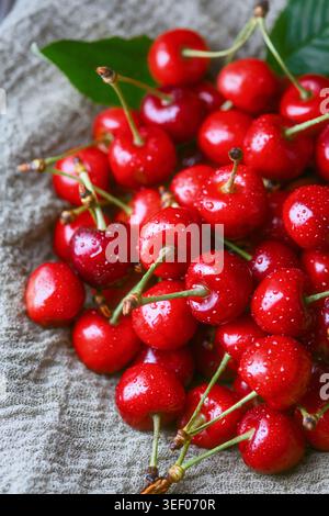 Cerises fraîches avec des feuilles vertes sur une surface texturée claire. Fruits rouges brillants mûrs, produits biologiques d'été Banque D'Images