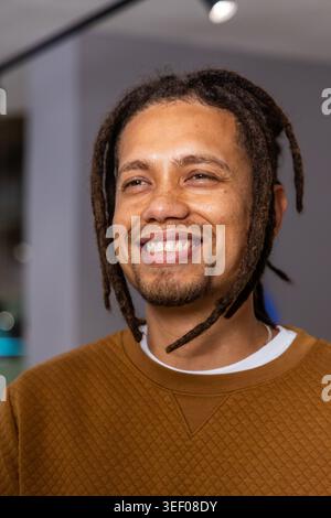 Homme afro-américain souriant, portant un top matelassé marron et un collier de chaîne dans les projecteurs de la galerie Banque D'Images