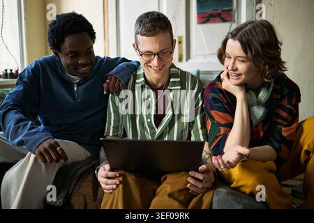 Jeunes adultes multiethniques collaborant sur ordinateur portable tout en étant assis ensemble, discutant de contenu en ligne et de travail d'équipe. Utile pour l'apprentissage à distance, la culture des startups, la communication numérique Banque D'Images