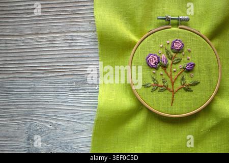 Cerceau de broderie avec broderie florale faite à la main sur tissu vert, vue rapprochée de l'artisanat d'aiguille et de la texture textile. Concept de bricolage traditionnel Banque D'Images