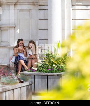 Deux femmes utilisant des smartphones alors qu'elles étaient assis à l'extérieur à Mayfair, Londres. Banque D'Images