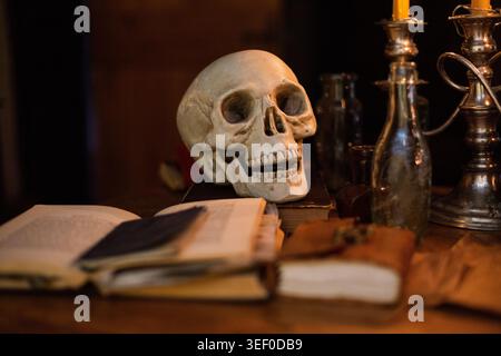 Un crâne est assis sur une table dans une pièce sombre, entouré de cahiers et de chandeliers Banque D'Images