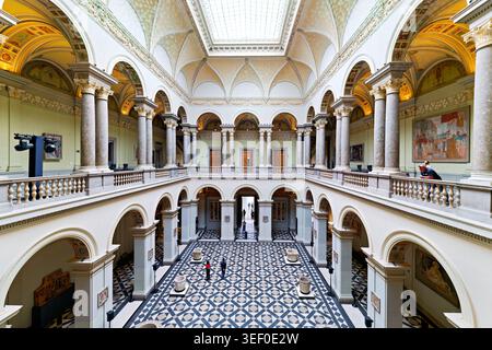 Les visiteurs explorent le Musée des Beaux-Arts de Budapest. La salle montre un haut plafond et des colonnes détaillées. Des œuvres d'art bordent les murs. Banque D'Images