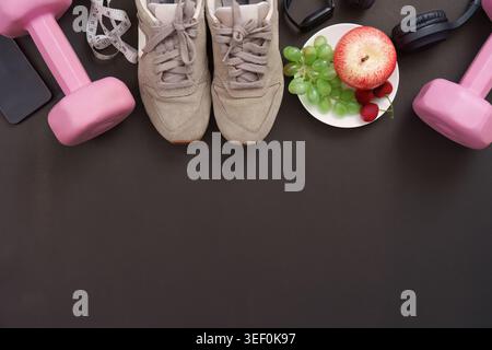 Équipement de fitness avec des fruits sains et des baskets sur fond sombre Banque D'Images