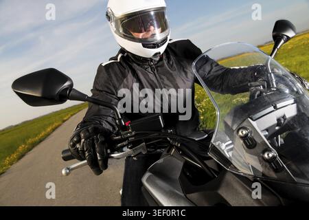 Motard en casque et veste en cuir roulant sur la route Banque D'Images
