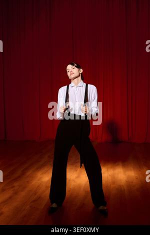 Une femme artistique exprime gracieusement son talent dans un théâtre, entourée de riches rideaux rouges. Banque D'Images