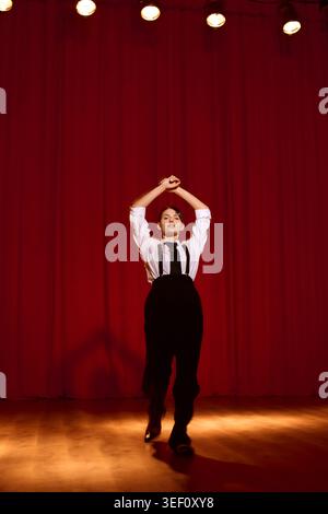 Une jeune femme exprime son art sur scène sous des lumières chaudes avec un fond rouge vif. Banque D'Images