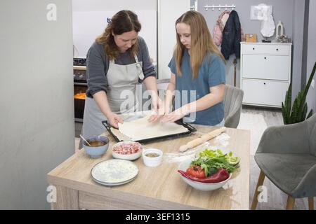 Fille joyeuse et mère cuisinant des pizzas italiennes ensemble dans une cuisine domestique confortable. Famille préparant la nourriture à la maison Banque D'Images
