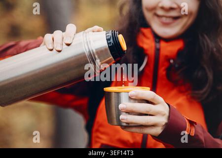 Femme souriante verse la boisson chaude du thermos en métal dans la tasse à l'extérieur. technologie d'isolation sous vide, ingénierie d'efficacité thermique, produit fonctionnel Banque D'Images