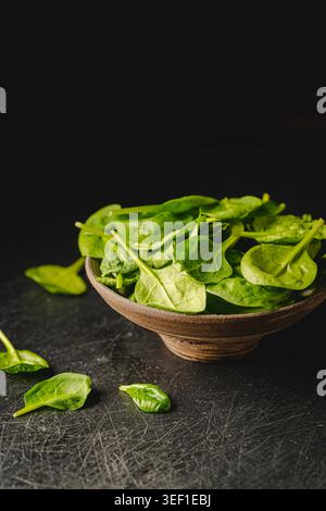 Feuilles d'épinards frais sur boel foncé sur fond noir. Nourriture végétalienne saine. Banque D'Images