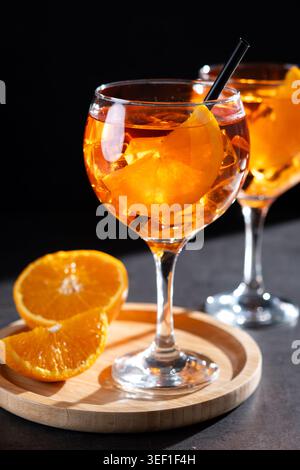 Gros plan de deux cocktails Aperol Spritz servis avec des glaçons, des tranches d'orange et des pailles noires dans d'élégants verres à pied. Apéritif d'été orange vif Banque D'Images