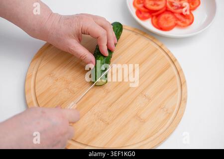 Trancher le concombre frais sur une planche à découper en bois, gros plan de la préparation des aliments dans la cuisine. Banque D'Images
