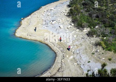 Plan en grand angle de personnes marchant le long du littoral sablonneux et incurvé d'un lac ou d'un réservoir turquoise Banque D'Images