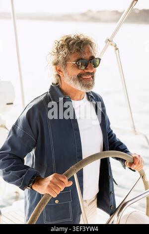 Homme dirigeant bateau, souriant et portant des lunettes de soleil, profitant de la voile d'été Banque D'Images