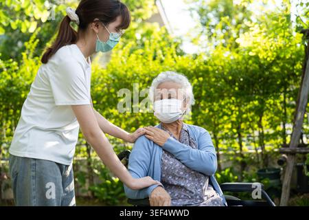 Aidants aidez et soignez le patient asiatique senior portant un masque assis sur un fauteuil roulant dans le service hospitalier de soins infirmiers, concept médical solide et sain. Banque D'Images