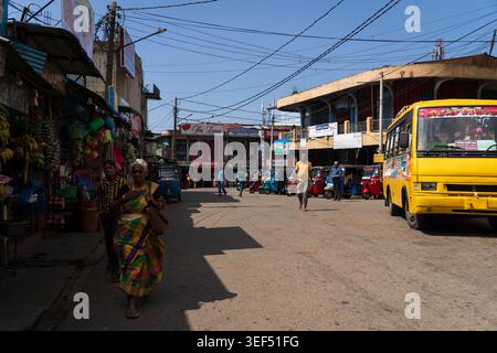 Femme locale dans un saree traditionnel marchant dans une rue animée avec un bus jaune et des magasins dans la ville de Haputale, Sri Lanka Banque D'Images