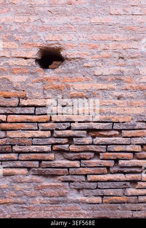Rome, Italie : texture de l'ancien mur de briques rouges altérées avec détail de trou rond unique au Colisée romain. Fond de surface de ruines archéologiques. Banque D'Images